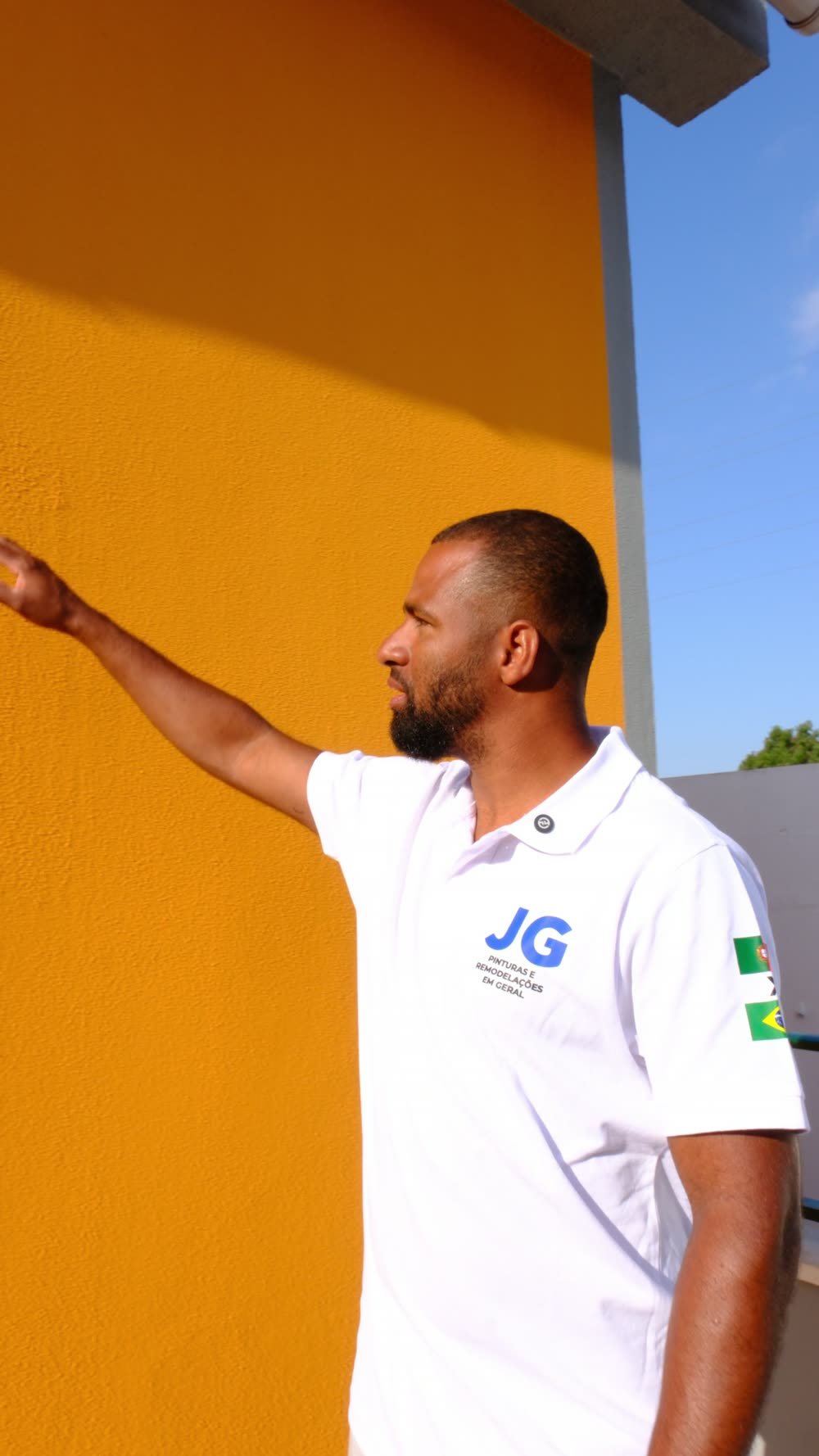Gleidison Freitas, responsável da JG Pinturas, de polo branco da empresa, junto a uma fachada laranja acabada
