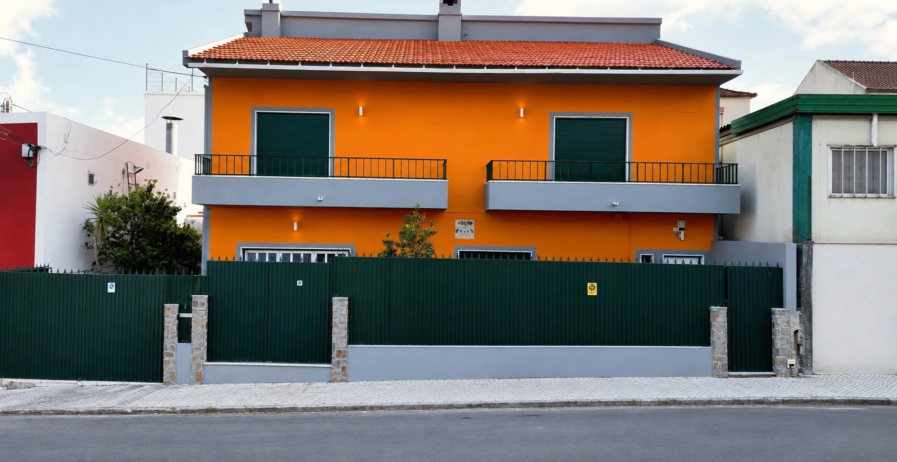 Moradia de dois pisos com fachada pintada de laranja, portadas e portão verde-escuro, molduras cinzentas e telhado cerâmico — obra da JG Pinturas em Lisboa e Região