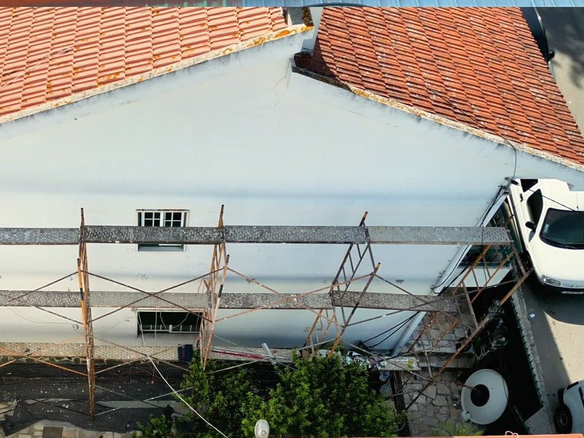 Cobertura da moradia antes da obra: telha envelhecida com musgo e andaimes montados