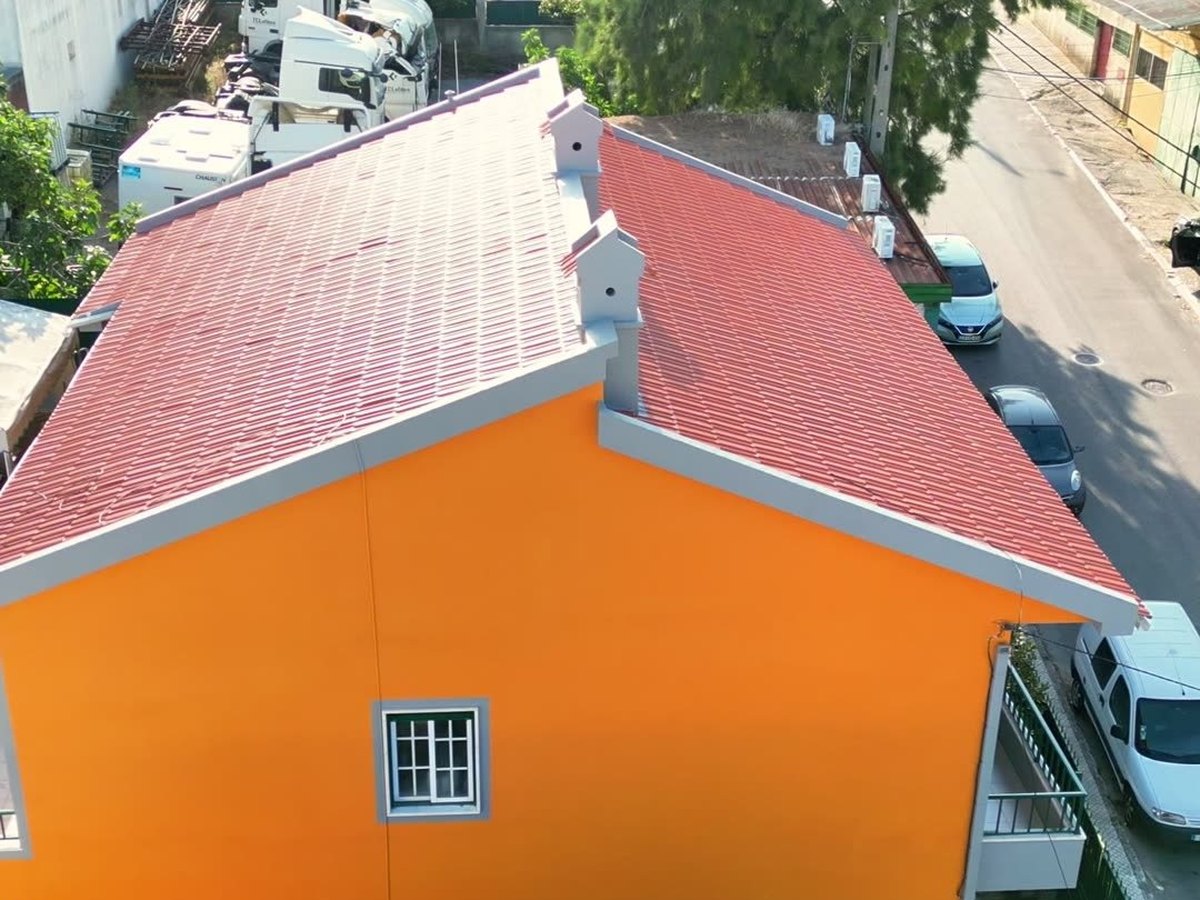 A mesma moradia depois: telhado tratado, fachada laranja uniforme e beirais brancos definidos